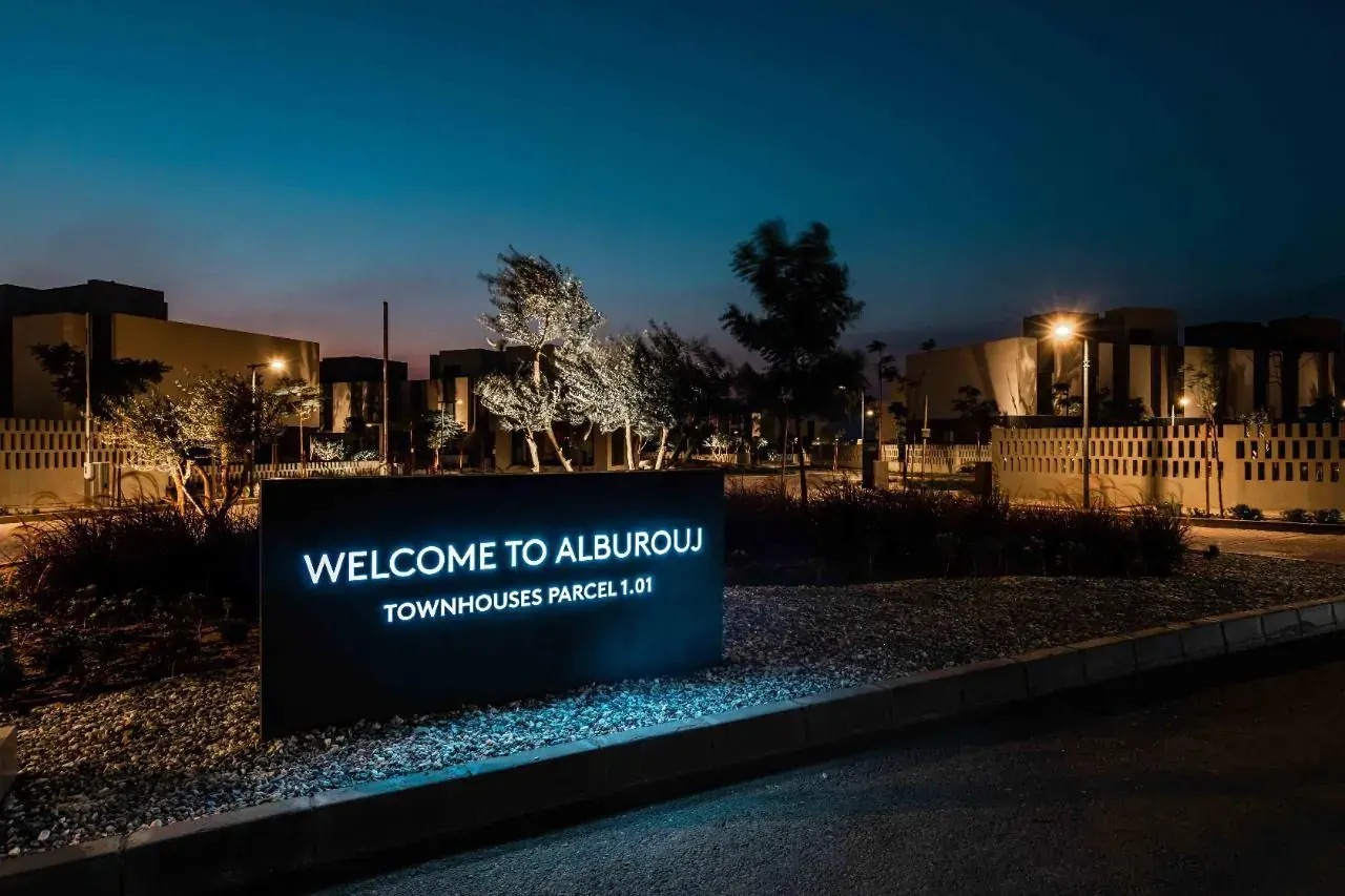 Illuminated Welcome to Al Burouj sign at dusk